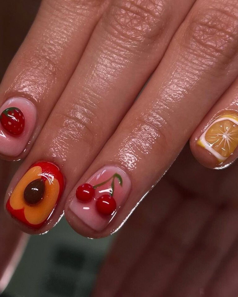 Close-up of a hand with vibrant nail art with fruit, featuring various fruit designs. The nails display detailed depictions of cherries, strawberries, an orange slice, and an avocado on a glossy finish.