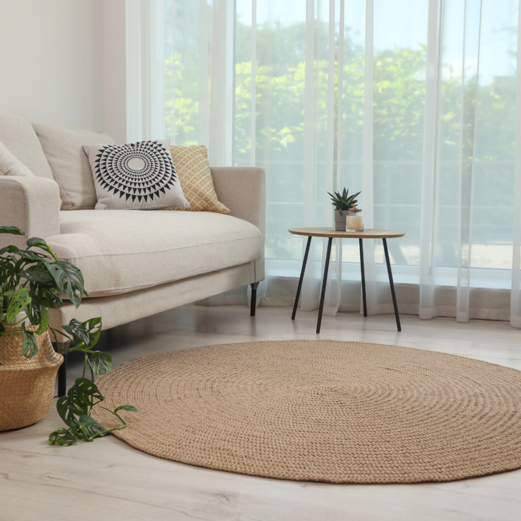 Bright and airy living room with a beige sofa, accent pillows, a round jute rug, and greenery, offering a perfect example of how to decorate a living room with natural textures and minimalist charm.