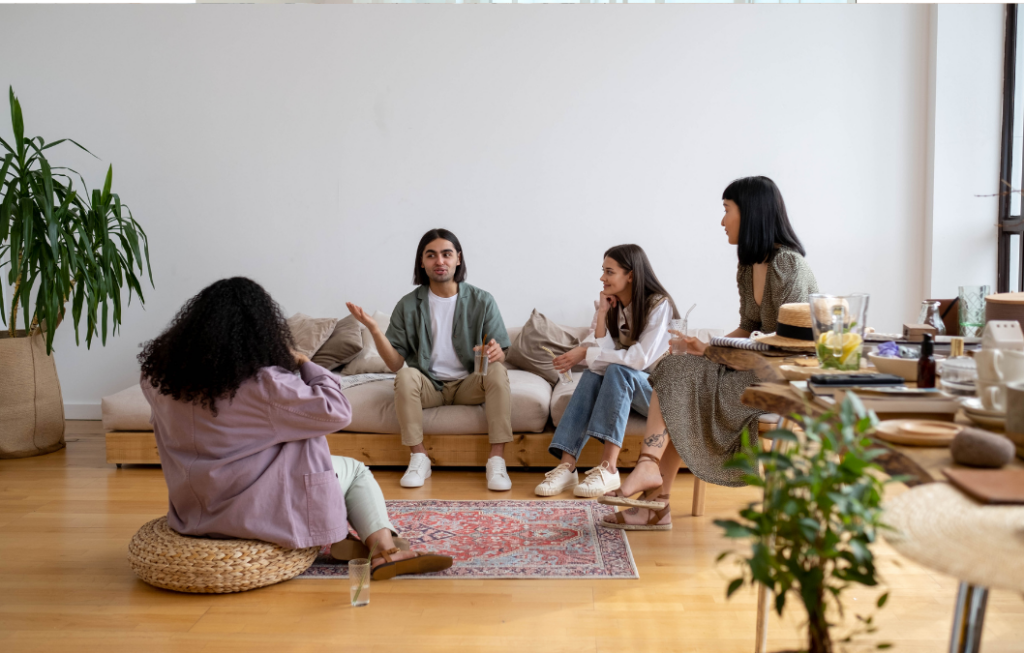 Four individuals engaging in conversation in a stylish and serene living room, showcasing ideas on how to decorate a living room with neutral tones, comfortable seating, a patterned rug, and natural elements like plants.