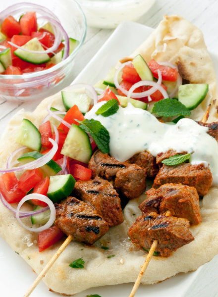 A delicious plate of kebab skewers served on naan bread, topped with fresh cucumbers, tomatoes, onions, and yogurt sauce, from a hidden gem restaurant in DC specializing in Mediterranean cuisine.