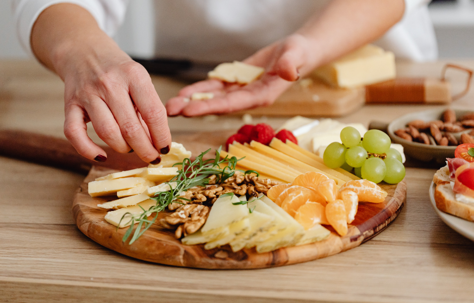 Person arranging a variety of cheeses, nuts, fruits, and herbs on a wooden platter, demonstrating creative ideas on how to make a charcuterie board for an elegant party spread.