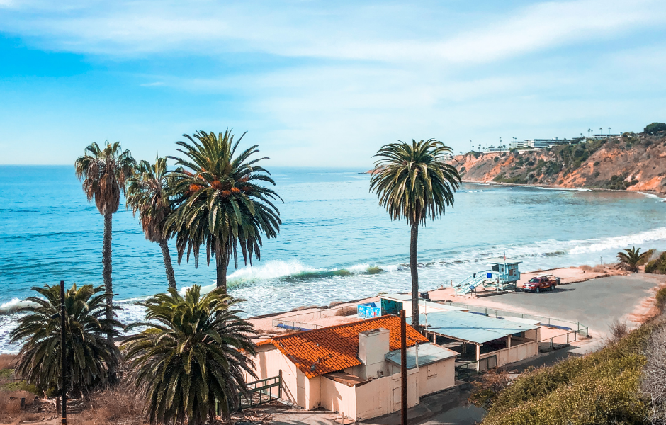 A scenic view of Grayton Beach 30A featuring palm trees, blue ocean waves, and a charming coastal building under a bright sky.