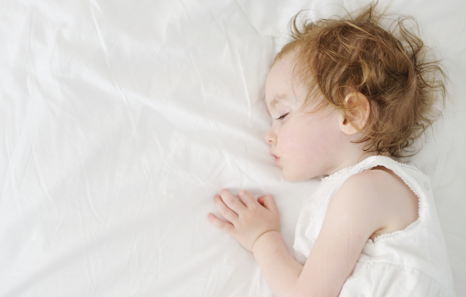 A peacefully sleeping toddler on a white bed, illustrating a restful night after following tips on how to put a toddler to sleep.