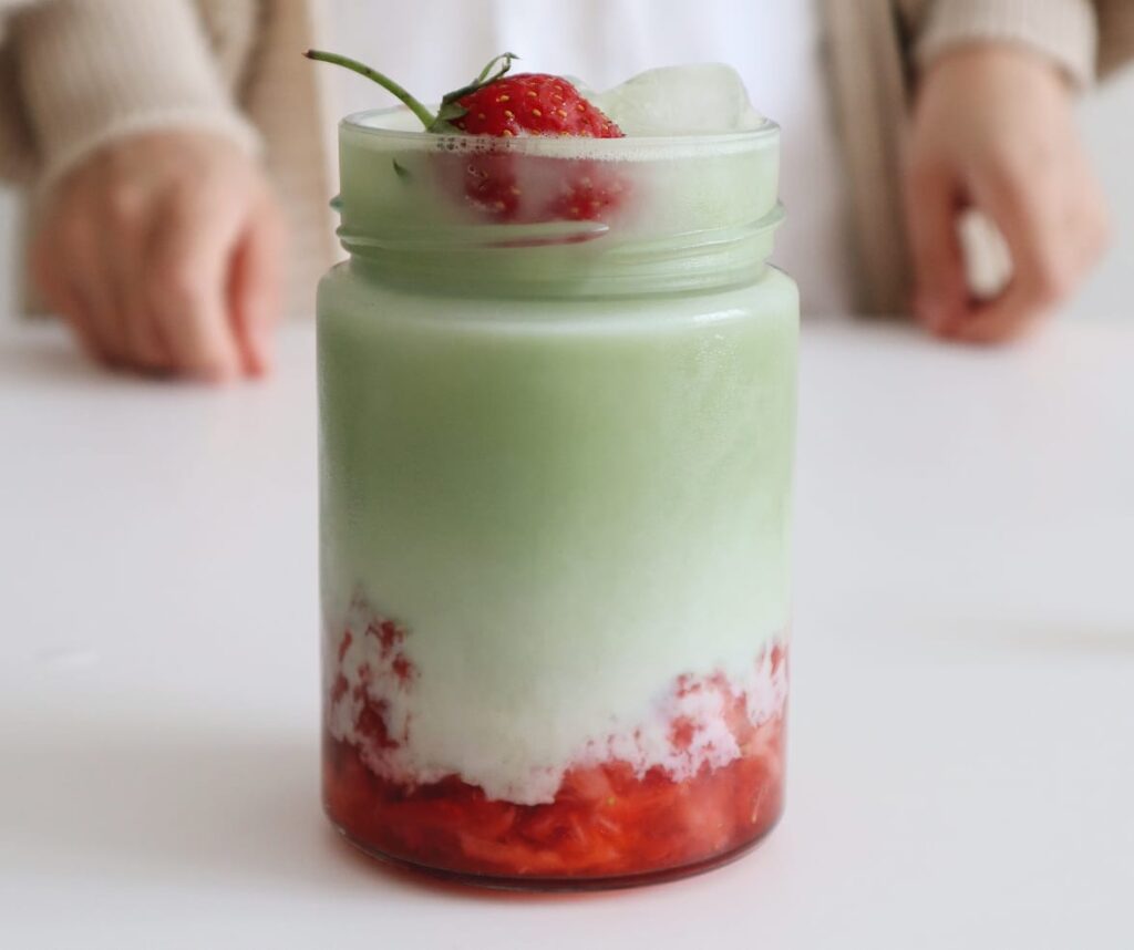 Layered matcha latte with strawberries in a glass jar. The Ultimate Dalgona Matcha Latte Recipe: Boost Your Health and Savor Every Sip.
