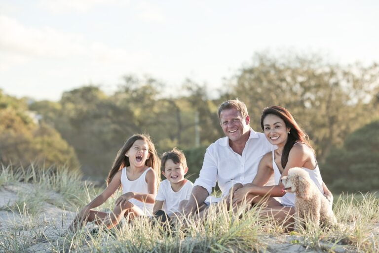 Image of a family sitting in fall settings, containing a mom, dad, a boy, and a girl, all wearing white outfits, represnting fall family photo outfits