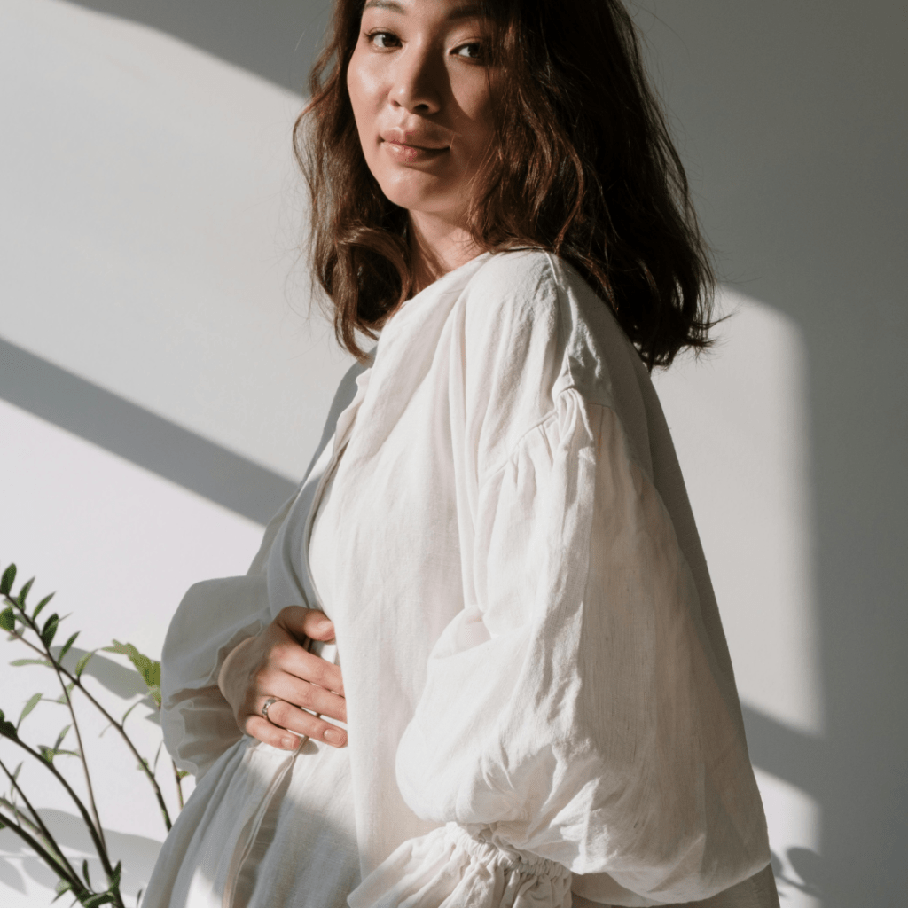 Close-up image of a lightweight, sheer long-sleeve blouse in white. The blouse has a delicate, airy appearance with a slightly translucent fabric, making it ideal for layering or wearing on warm days. The sleeves are long and flowy, adding to the elegant and breezy look of the garment. Image used for the article A Must-Have for Chic Maternity Capsule Wardrobe Spring.