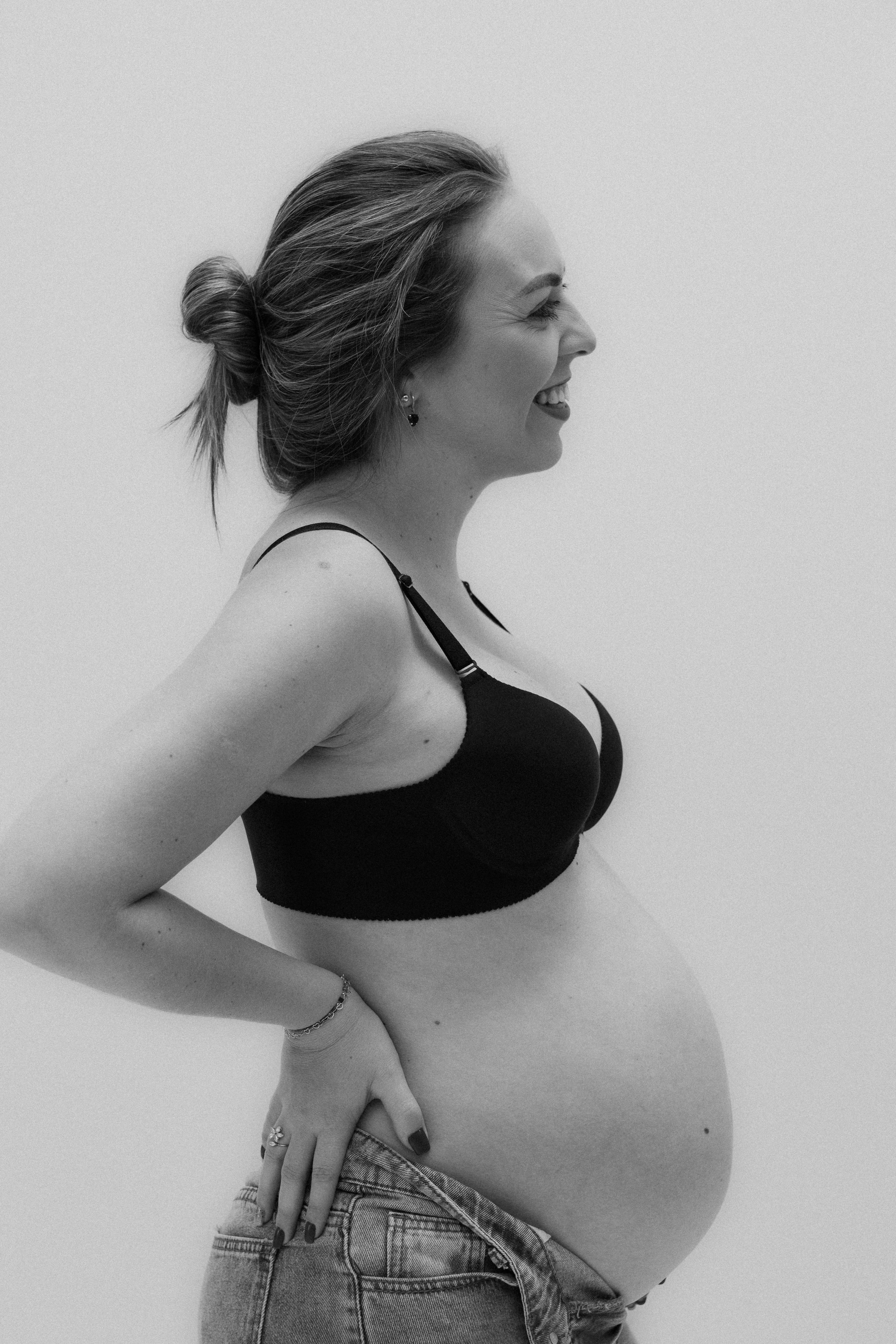 Image of a woman with their hair tied in a bun. The person is wearing a black sports bra and appears to be in motion, possibly jogging or exercising. The image is slightly pixelated, which gives it a grainy texture. The background is plain and light-colored, making the subject stand out clearly. Image used for the article Pregnancy Capsule Wardrobe Basic.