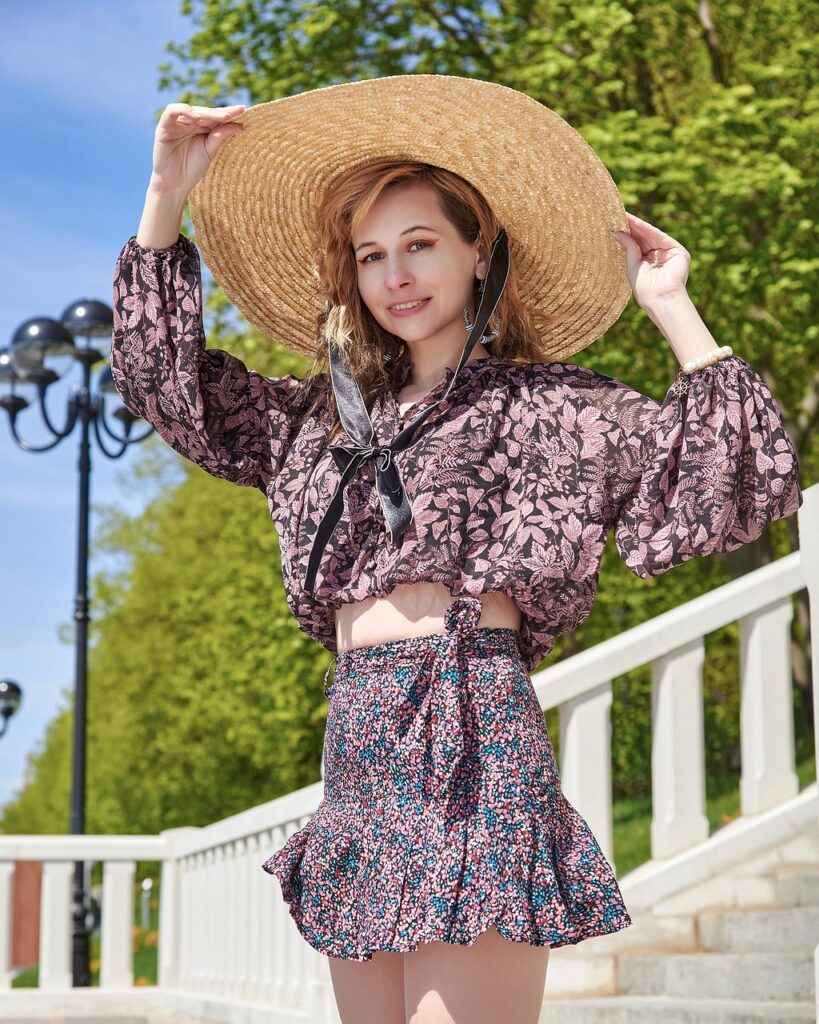 Close-up image of a young woman is standing against a plain background, wearing a stylish floral dress with puffed shoulder sleeves. She has long, flowing hair and a gentle smile on her face. The dress features a vibrant pattern, adding a touch of elegance to her look. Her relaxed posture and the simplicity of the background highlight her outfit beautifully. Image used for the article How to Dress in Your 30s.