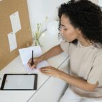 A lady in white dress sitting and writing something on the page. Image used for the article daily routine for working moms