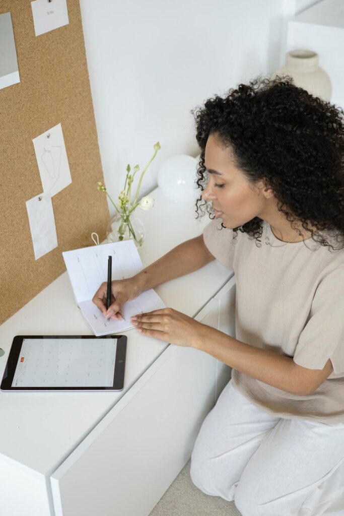 A lady in white dress sitting and writing something on the page. Image used for the article daily routine for working moms