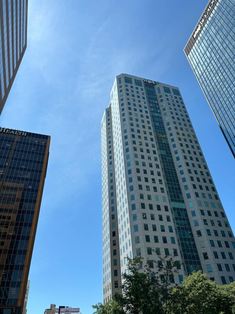 Image of several tall, modern skyscrapers viewed from below, set against a clear blue sky. The buildings feature a mix of glass and concrete facades, reflecting the sunlight. One of the buildings prominently displays the name "PNC" near the top. Trees can be seen in the foreground, adding a touch of greenery to the urban setting. Image used for the article Things to do in Huntsville.