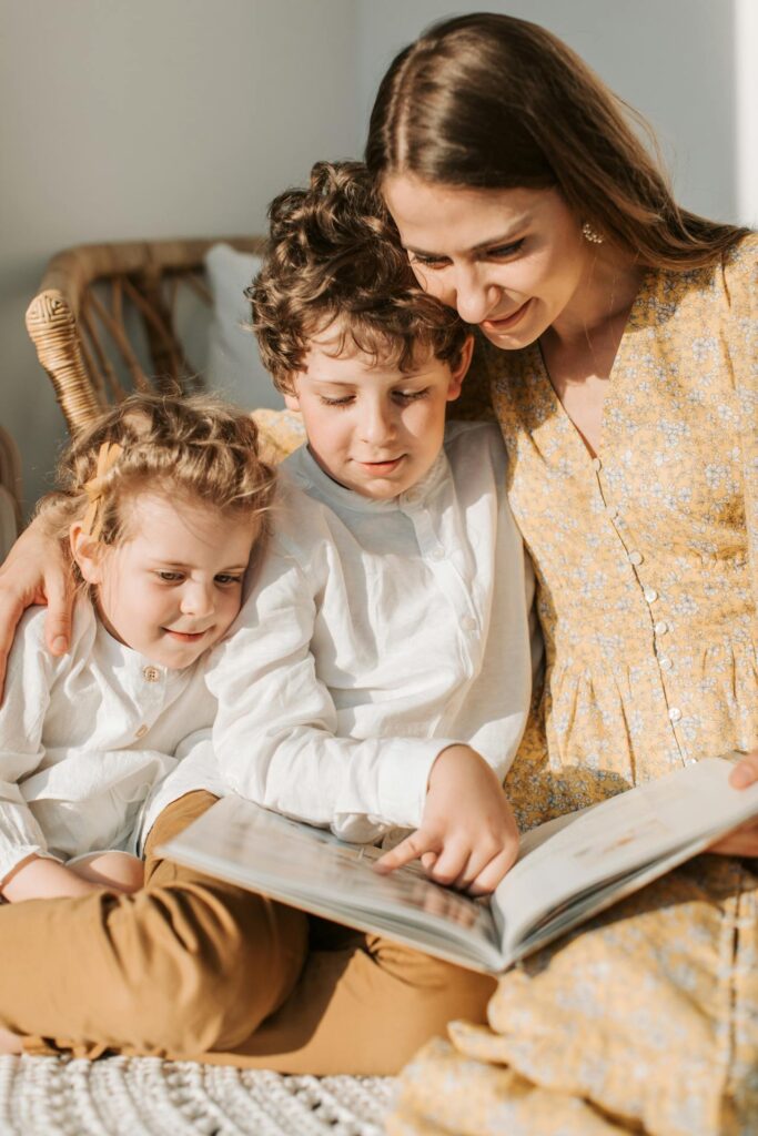 Image of a mother sitting with her two children, reading a book together in a bright and cozy setting. The family is smiling and engaged, with warm natural light highlighting their faces showing the attributes of a good mother.