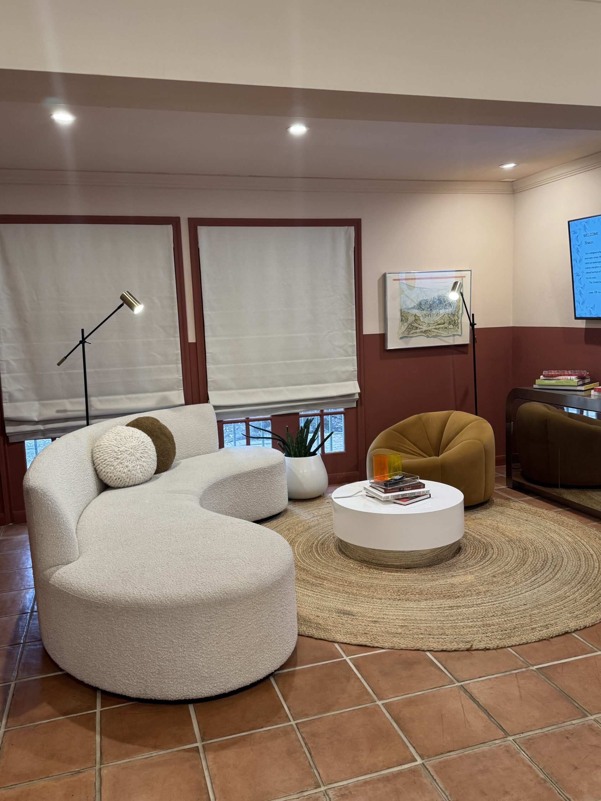 Image of a cozy living room with a curved white sofa, round coffee table, mustard accent chair, and warm tones.