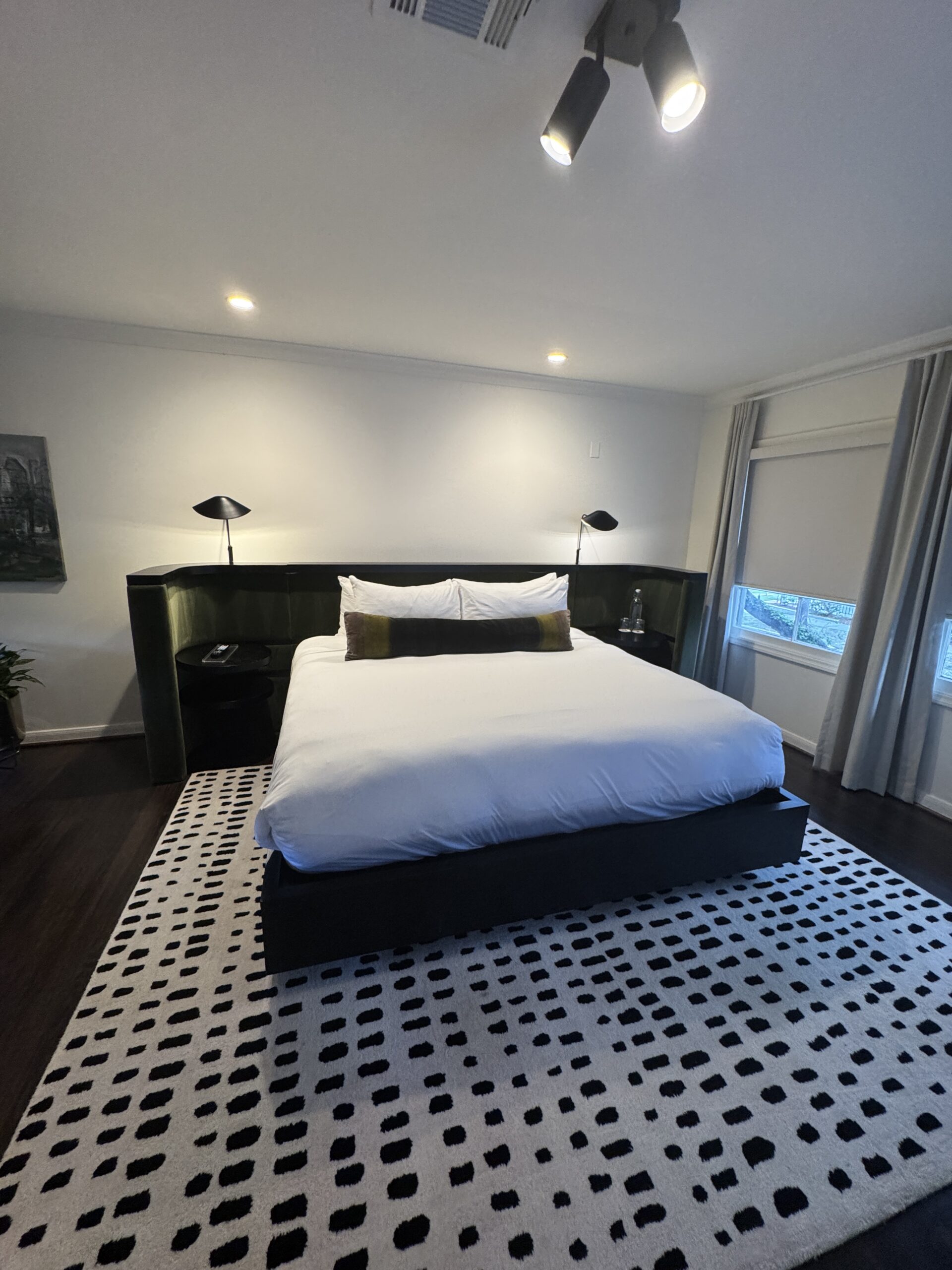 Image of a modern bedroom with a large bed, patterned rug, moody lighting, and sleek black decor elements, showing one day in Houston.