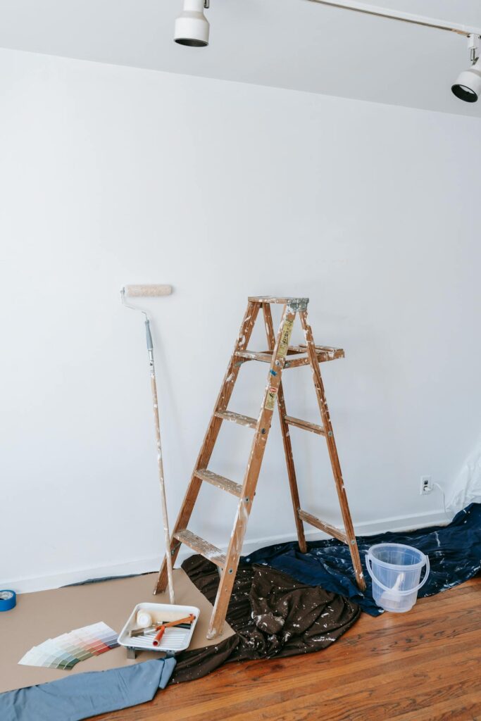 Image of a wooden ladder, paint supplies, and a white wall prepared for painting in a well-lit room representing ways for single moms to make money.