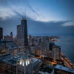 Image of a cityscape of Chicago at dusk, featuring the John Hancock Center and Lake Michigan, showing one day in Houston.