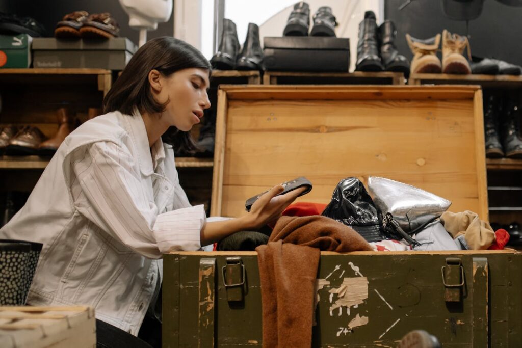 Image of a woman in a white jacket examines items in an open wooden chest filled with clothes showing wealthy single mom.