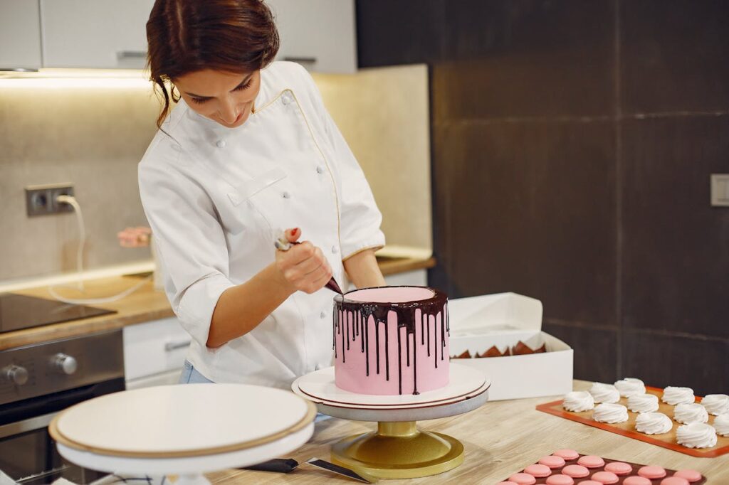 Image of a baker woman decorating a pink cake with chocolate drips in a professional kitchen representing single mom opportunities. 