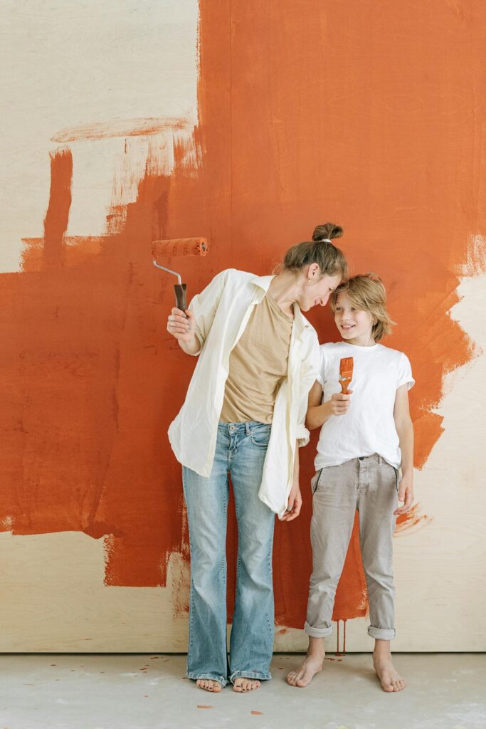 Image of a mother and child painting a wall orange together, sharing a happy and playful moment showing How to Make Extra Money as a Single Mom.