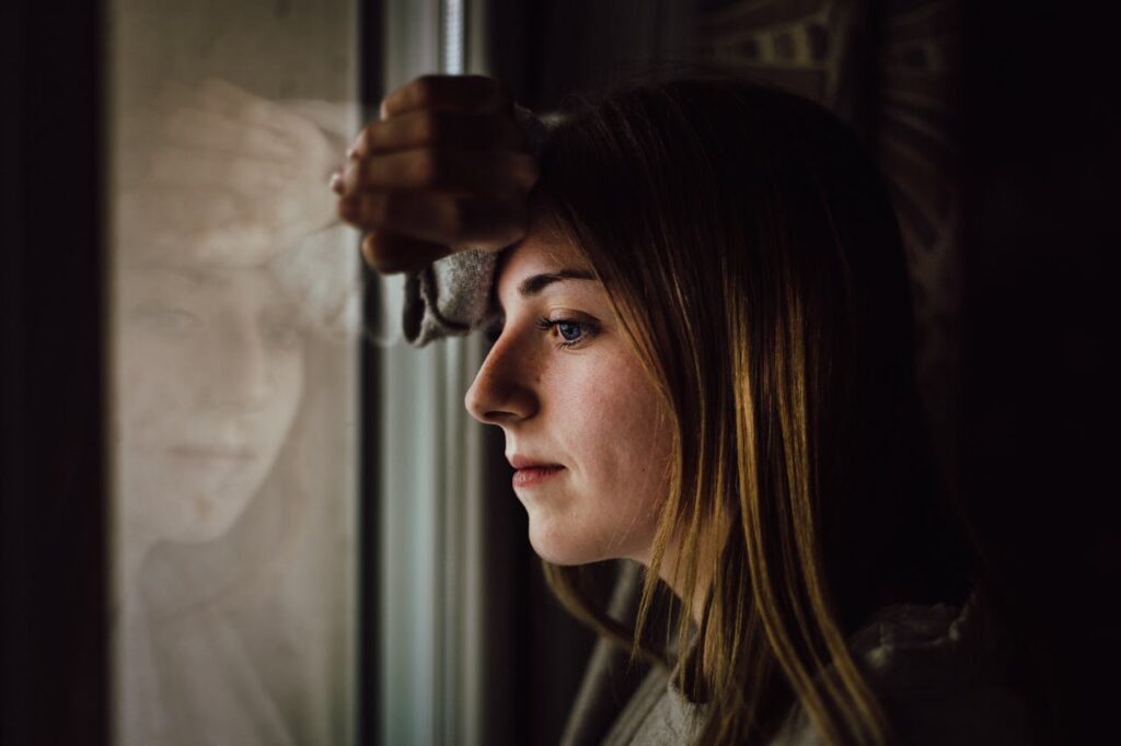 A woman staring thoughtfully out of a window, reflecting deeply while leaning against the glass representing can a stay-at-home mom collect social security disability?