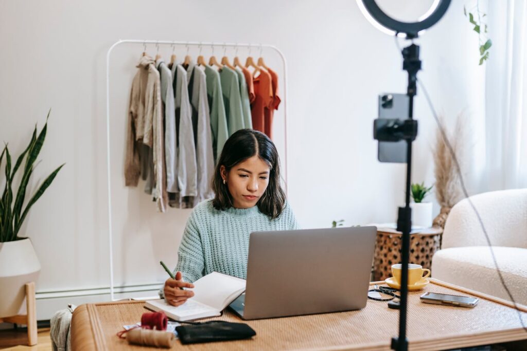 Image of a woman in a cozy room working on a laptop, surrounded by clothes and a ring light for filming showing How to be a single mom with no help.