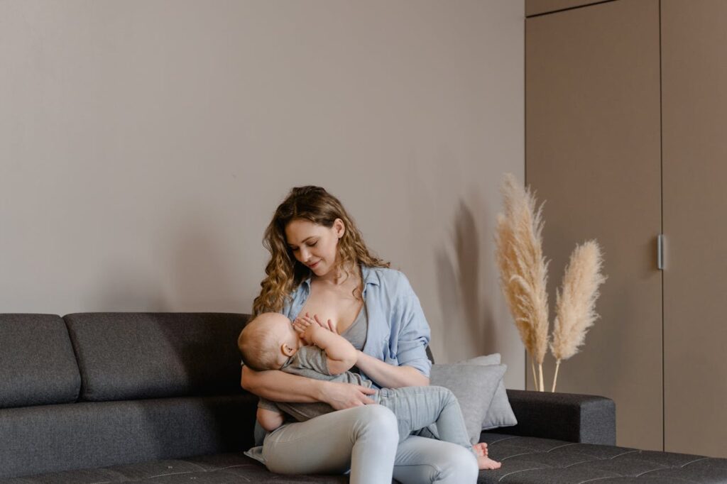 Image of a mother sitting on a sofa, breastfeeding her baby in a calm and cozy indoor setting, pampas grass nearby showing Lower Risk of Postpartum Depression.