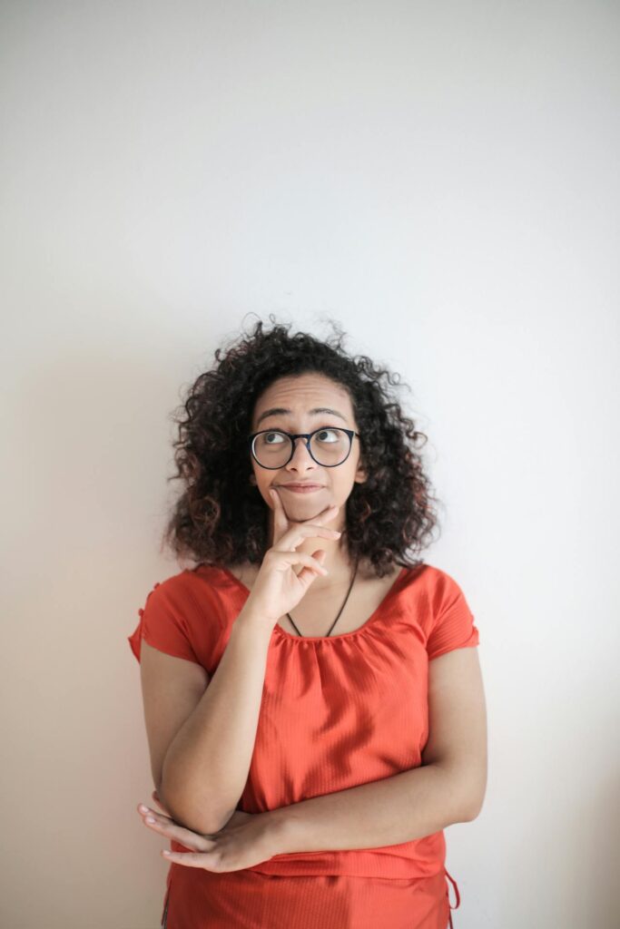 Image of a woman with curly hair wearing glasses and a red shirt, standing with a thoughtful expression showing disability insurance for stay-at-home parent. 