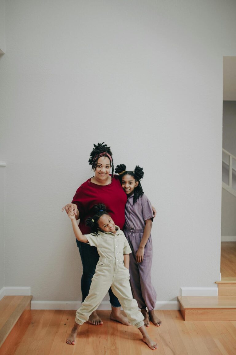 Image of a smiling mother with two daughters, posing together indoors near a staircase showing 10 best states that help single mothers