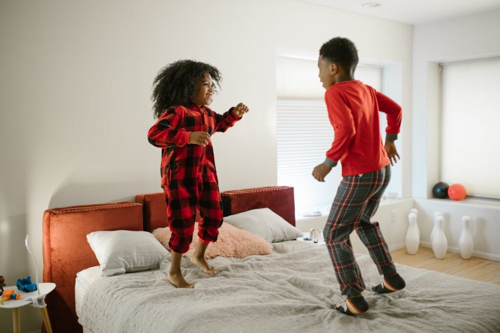 Close-up image of two children in pajamas joyfully jumping on a bed in a bright, playful bedroom setting, showing Working Mom Evening Routine.