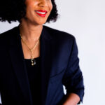 Image of a confident woman with short curly black hair in a blazer, smiling and looking to the side, showing how to be a working mom.