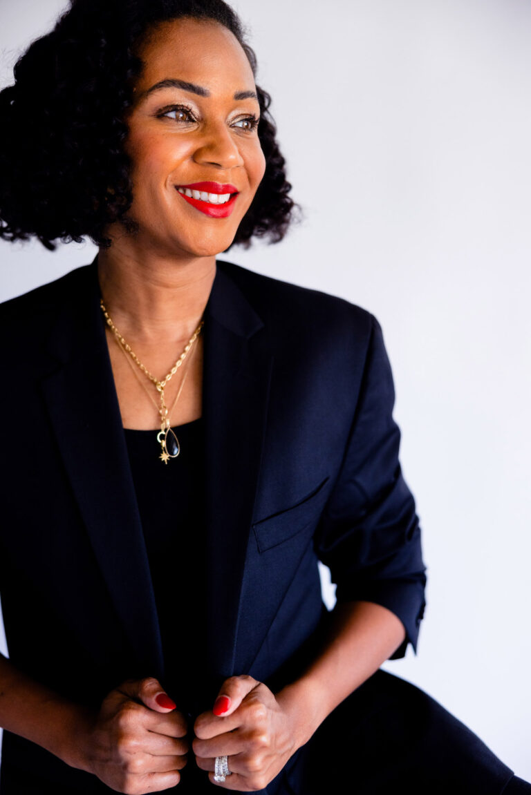 Image of a confident woman with short curly black hair in a blazer, smiling and looking to the side, showing how to be a working mom.