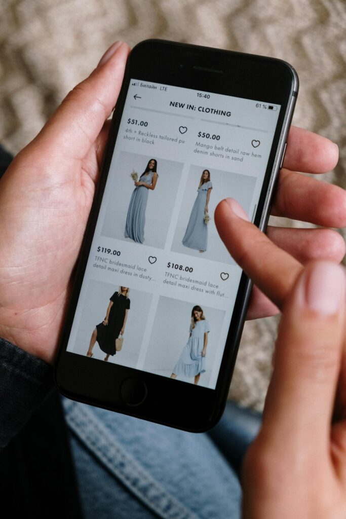 Image of a hand browsing a clothing shopping app on a smartphone, showing prices and dresses on the screen, showing shopping for plus-size clothes.