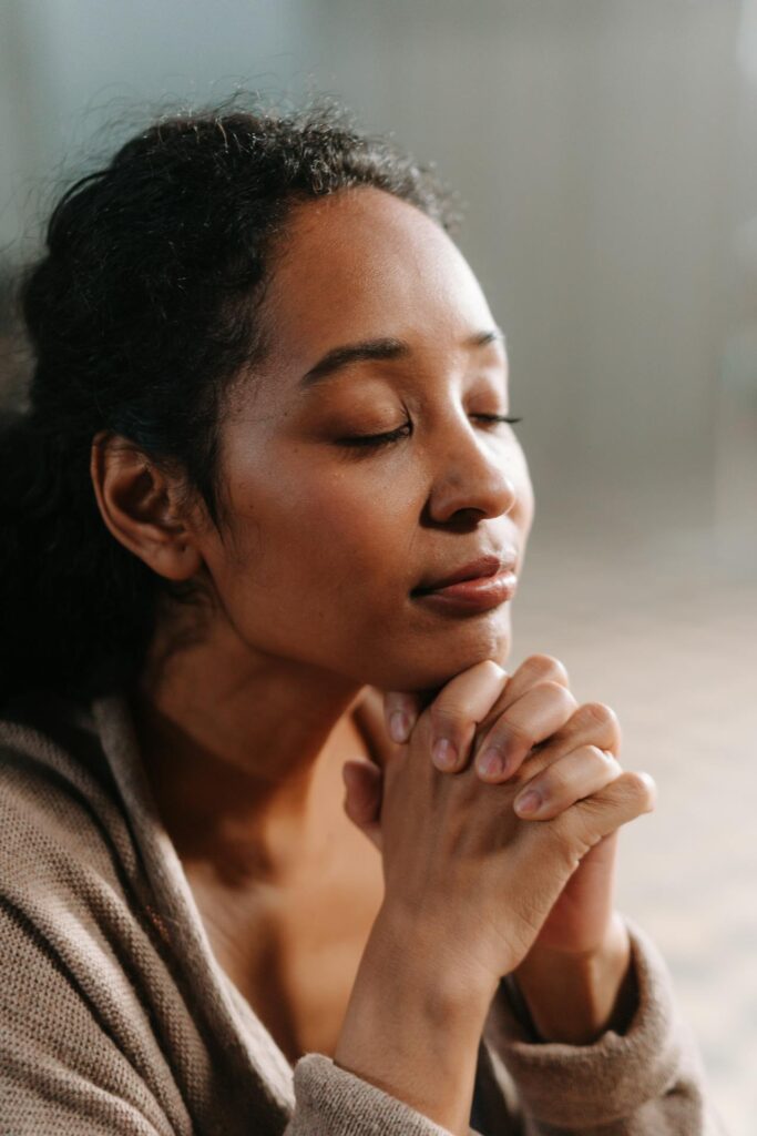 Close-up image of a  woman with closed eyes, resting her chin on her clasped hands in a moment of reflection.