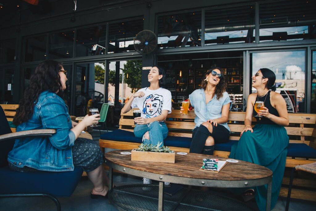 Image of four friends laughing and chatting at an outdoor café while enjoying drinks in a lively atmosphere.