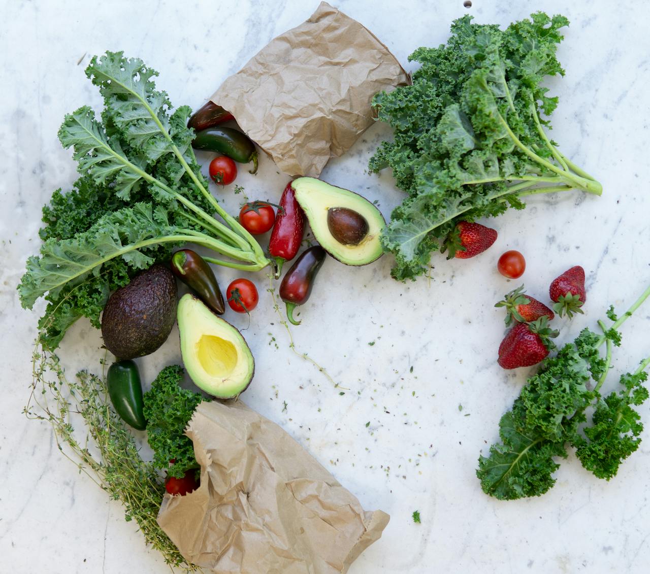 Image of fresh kale, avocados, chili peppers, strawberries, and tomatoes scattered on a marble surface, showing taking care of a colic baby.