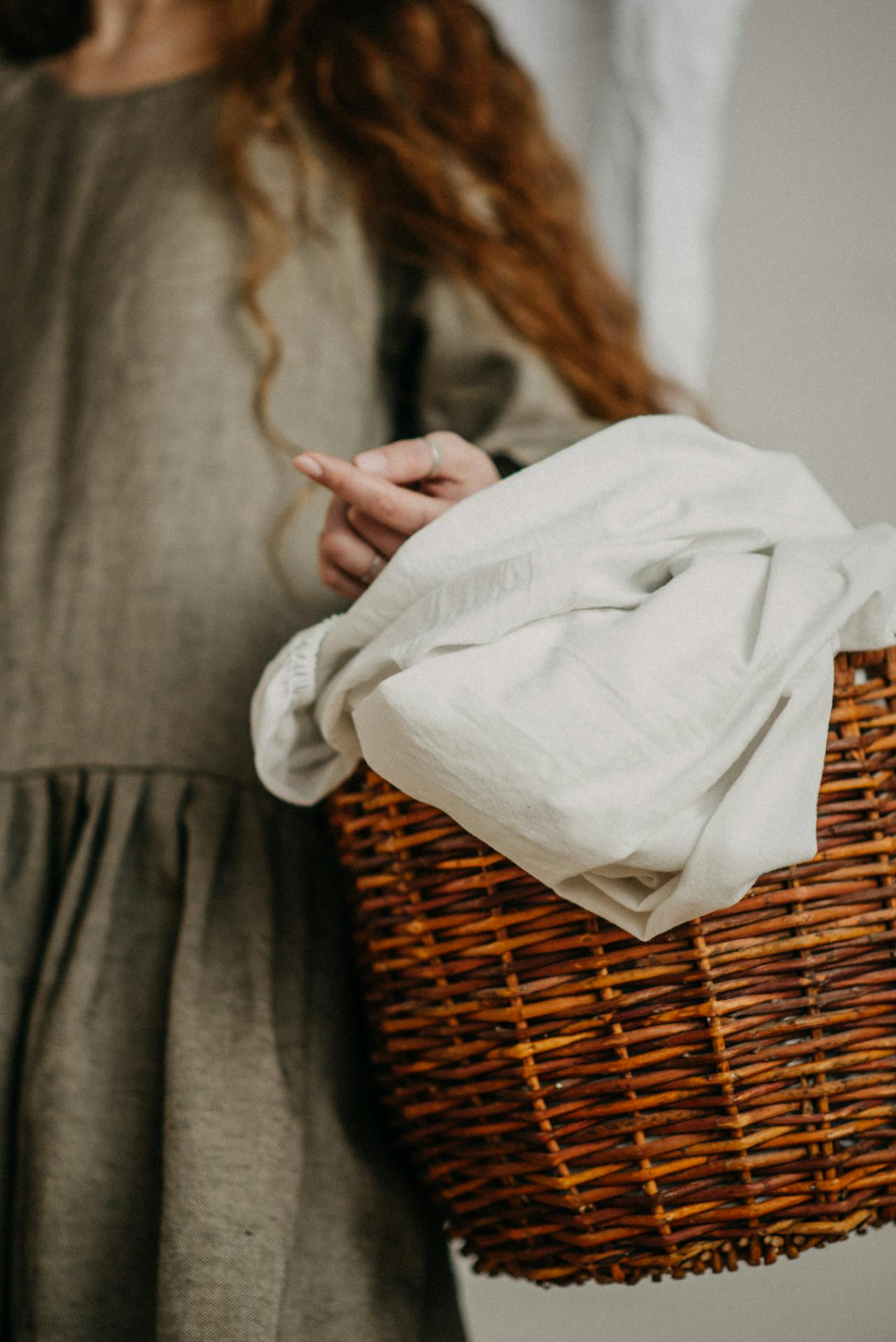 Image of a woman in a linen dress carrying a woven basket filled with freshly washed white sheets.