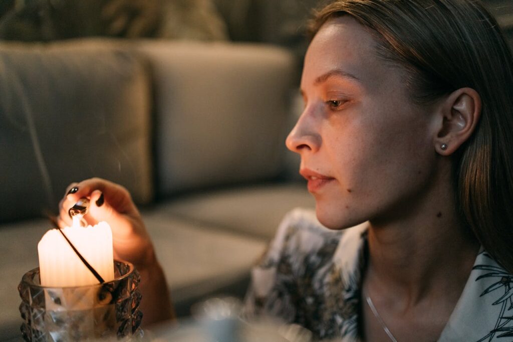 Image of a woman lighting a candle with a matchstick in a dimly lit room, creating a calm and cozy ambiance, showing work-life balance for moms.