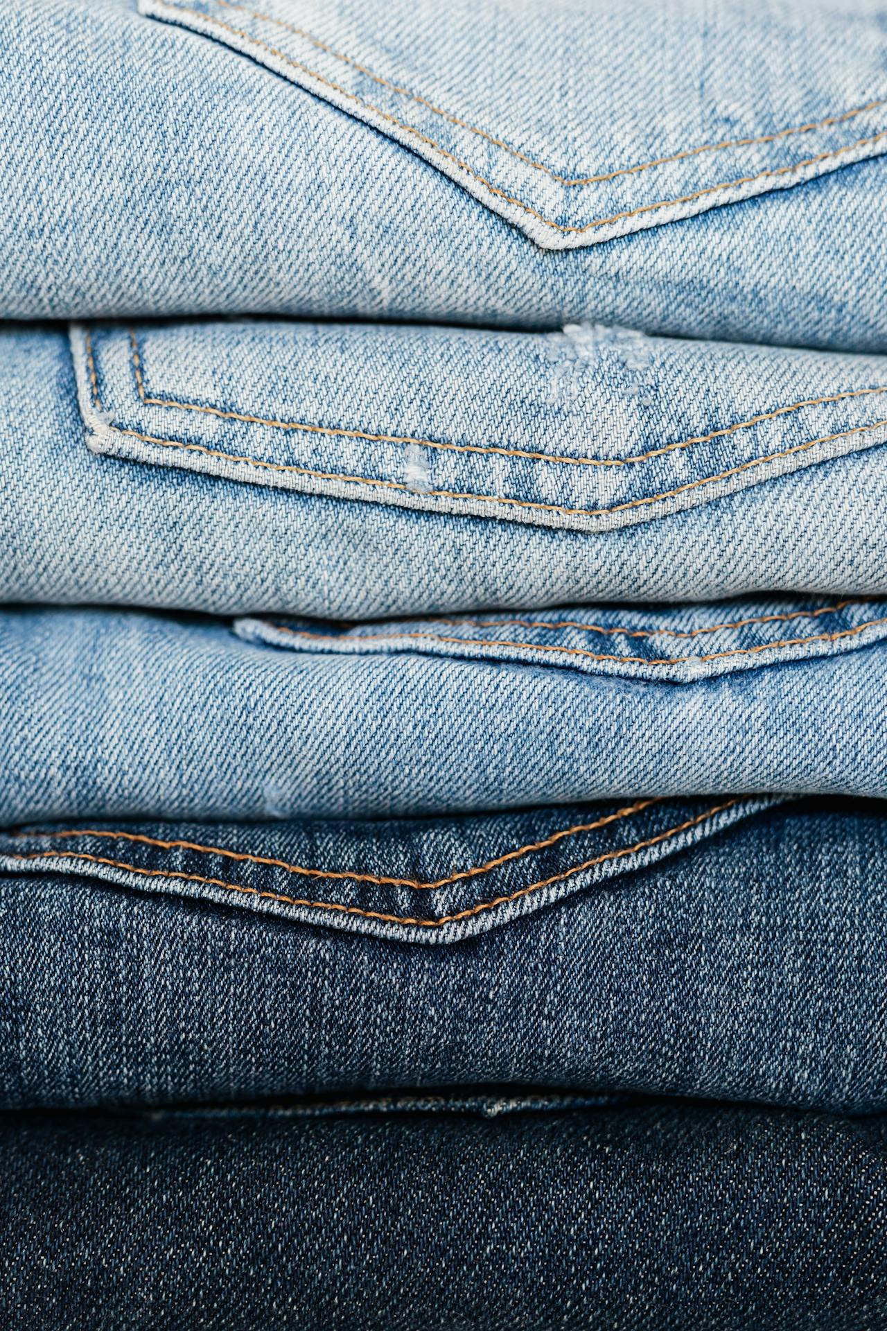 Image of a neatly stacked pile of denim jeans in various shades of blue, from light wash to dark indigo.