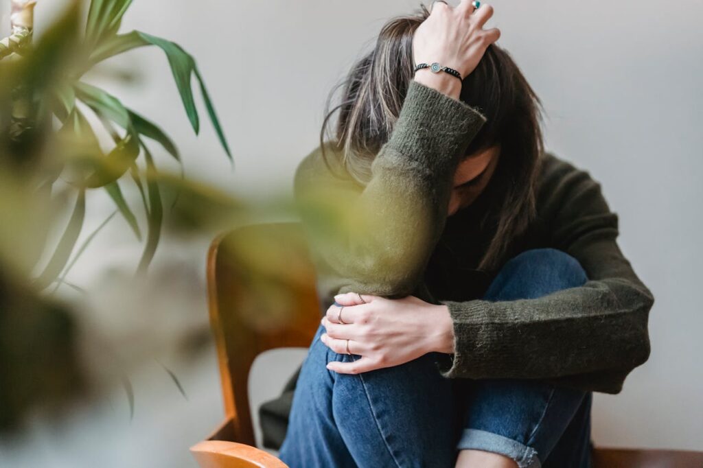 Image of a woman in a green sweater and jeans sits with her head in her hands, appearing distressed.