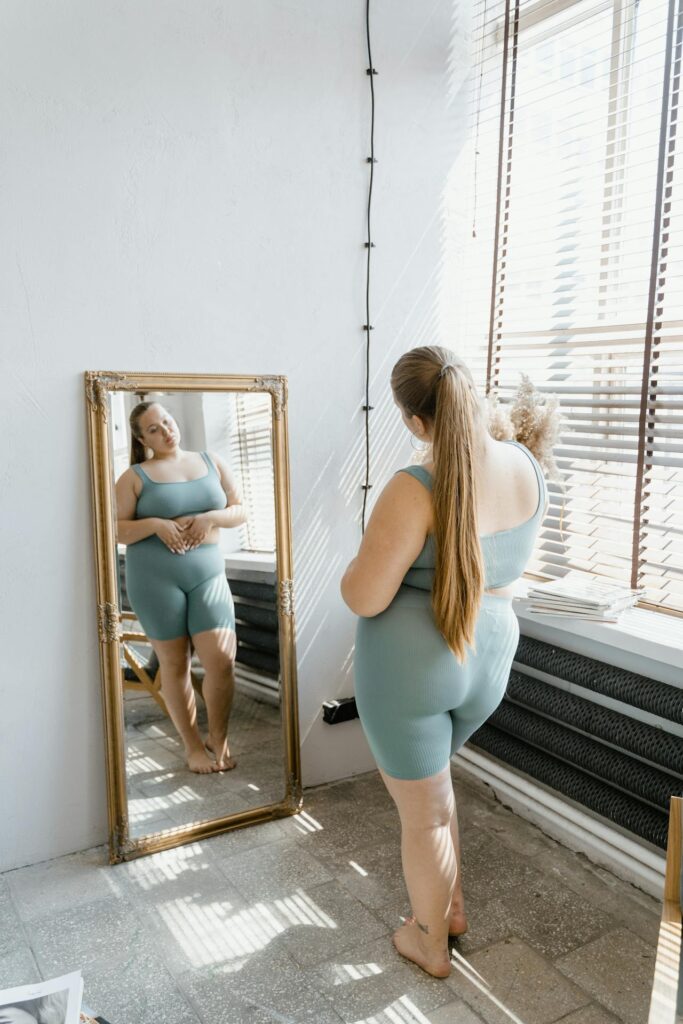 Image of a woman standing in front of the mirror checking on herself, showing plus-size mom fashion tips.