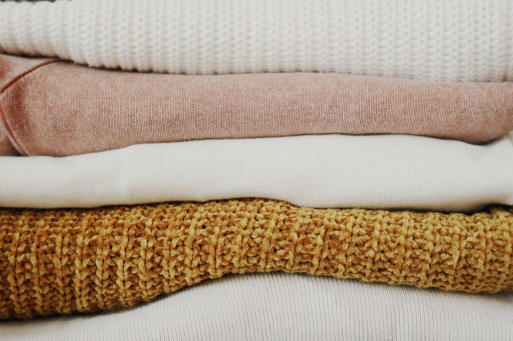 Image of a stack of neatly folded textured clothing in white, pink, and mustard tones on a flat surface, showing plus-size mom best friend.