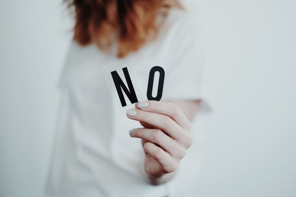 Image of a woman holding a cut-out card with the word 'NO' written in bold black letters on a white background.