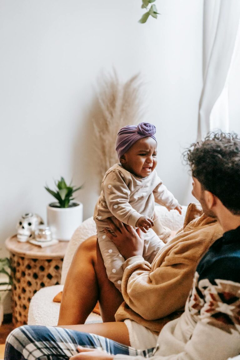 Image of a toddler wearing a purple headwrap and beige outfit crying while being held by an adult, showing breastfeeding mother eat to prevent colic.