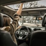 Image of a woman driving a Jeep with one hand on the wheel and the other reaching through the open sunroof, showing how long after giving birth can you drive.