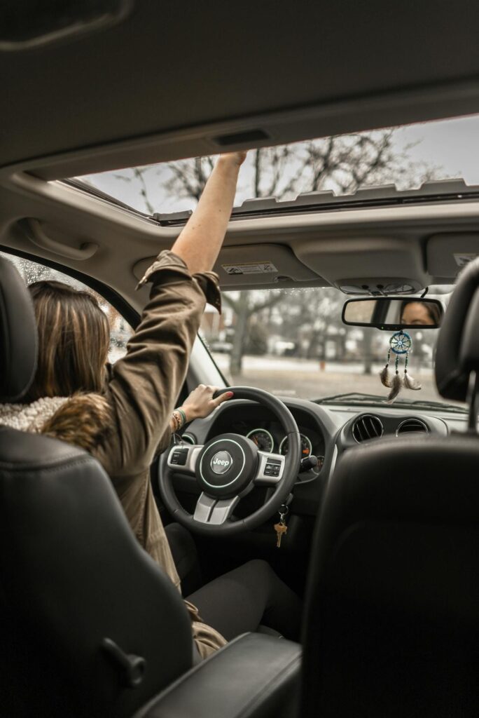 Image of a woman driving a Jeep with one hand on the wheel and the other reaching through the open sunroof, showing how long after giving birth can you drive.