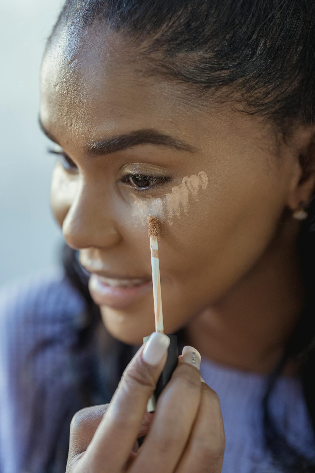 Image of a woman applies concealer under her eyes with a wand applicator, blending makeup on her smooth skin, showing mom style tips.