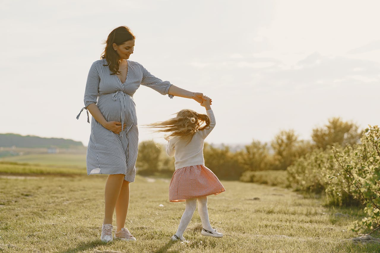 Image of a pregnant woman in a striped dress twirls her daughter in a field, enjoying a sunny outdoor moment, showing labor indicators.