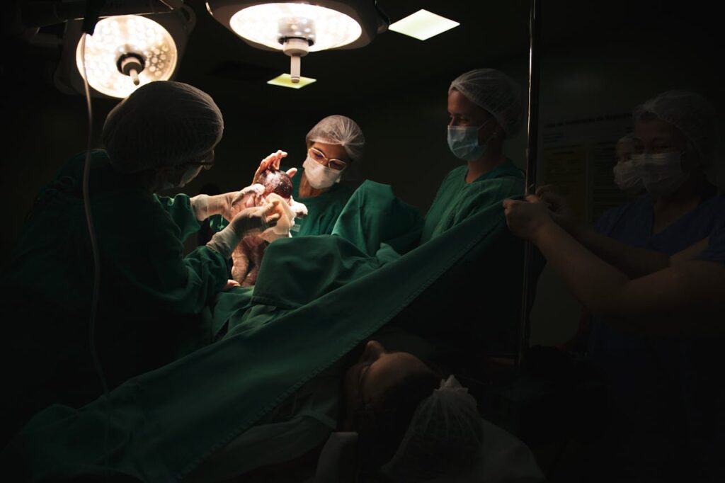 Image of a newborn baby is held by doctors in a dimly lit operating room during a C-section birth, showing driving after a c-section.