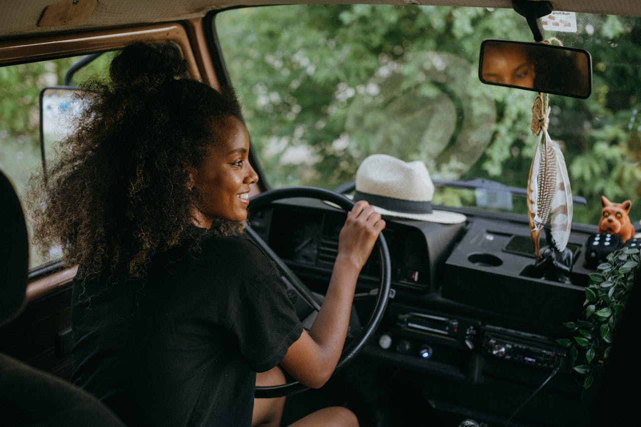 Image of a woman with curly hair driving a vintage vehicle, smiling while looking at the road ahead, showing how long to wait before driving postpartum.