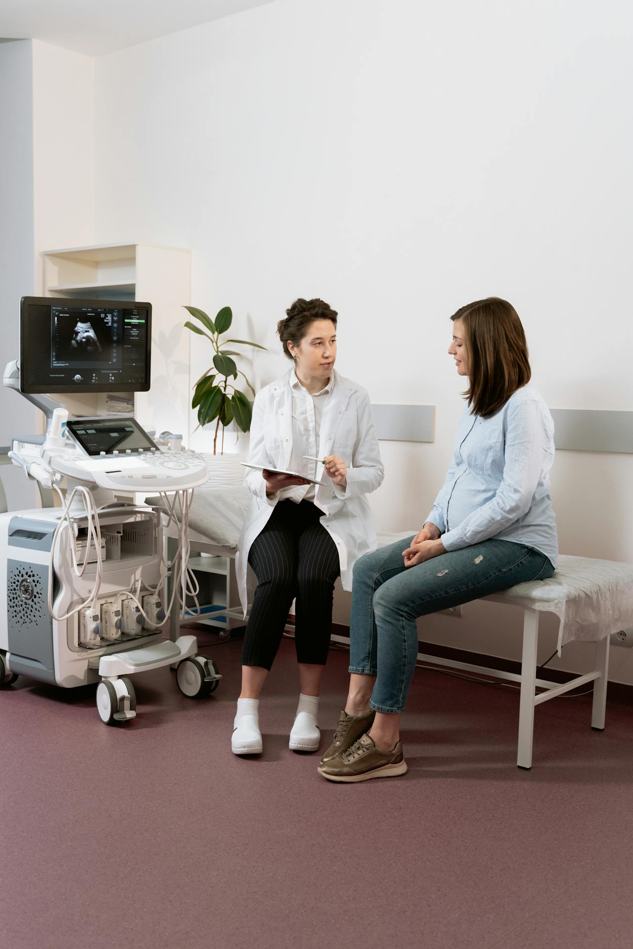 Image doctor in a white coat talks to a pregnant woman in casual clothes during an ultrasound visit, representing how to turn prodromal labor into real labor.